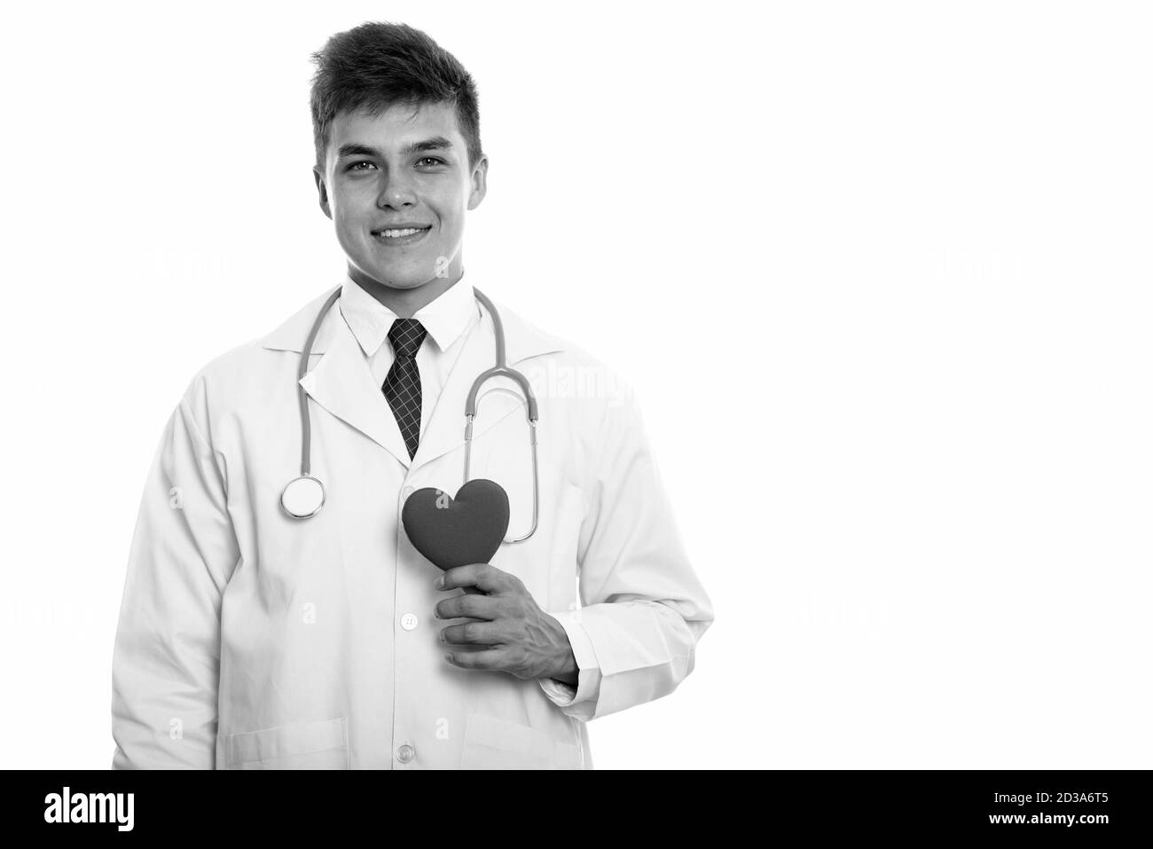 Studio shot of young happy man doctor smiling while holding red heart Stock Photo