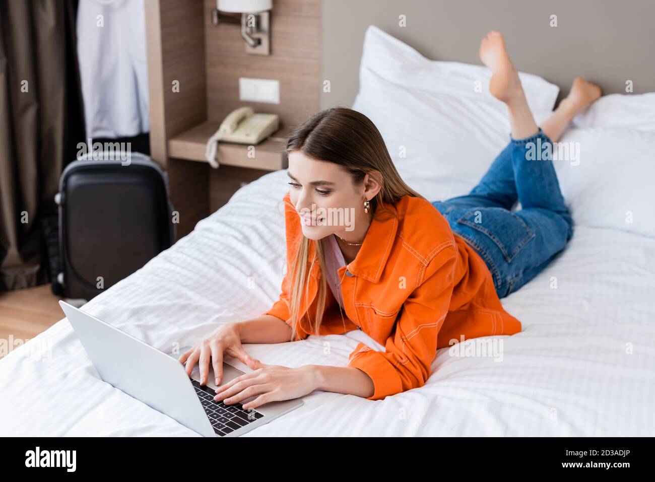 barefoot freelancer lying on bed and using laptop in hotel room Stock