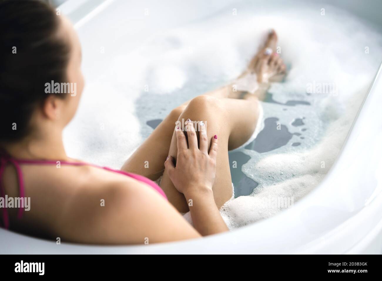 Woman in bath. Bathtub with bubbles and foam. Hand with nail polish in fingers after manicure. Clean and healthy skin. Skincare therapy and treatment. Stock Photo