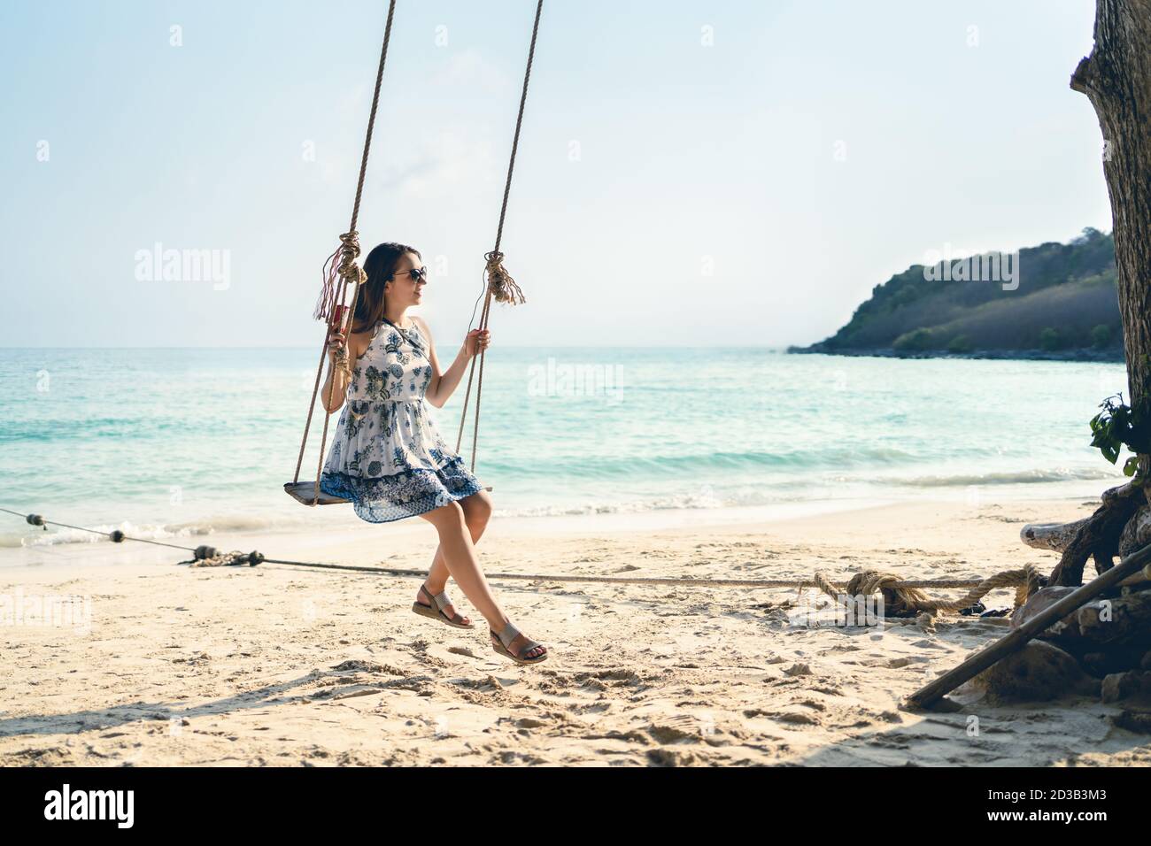 Swing in tropical paradise beach. Woman enjoying life and summer vacation on sunny island in Thailand. Pretty young lady in dress having fun. Stock Photo
