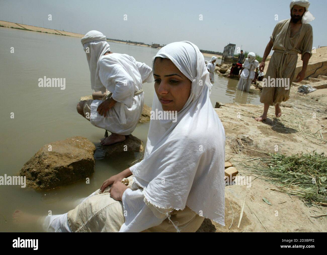 One of five Iraqi Mandean brides sits next to the Tigris river after her wedding ceremony in Baghdad June 8, 2003. Iraqi devotees of an obscure religion who take John the Baptist as their central figure perform virginity tests on their brides and take a dip in the murky Tigris river every Sunday to purify the soul.  Most of the world's 20,000 or so Mandeans live in southern Iraq and southwestern Iran. Stock Photo