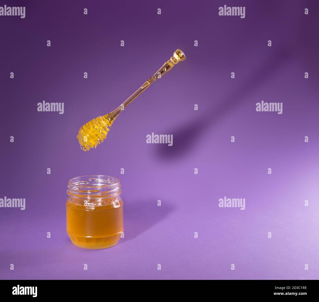 Honey dipper levitating above a jar of sweet natural honey on a purple