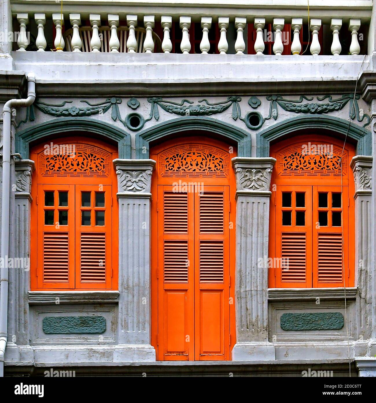 Restored Chinese peranakan shop house with orange wooden louvred shutters and ornate arches and architraves on a dark grey stone wall. Stock Photo