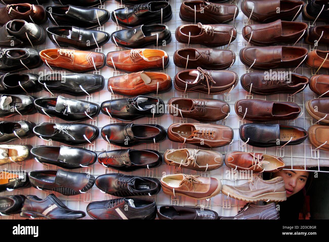 A Chinese vendor peers from behind an array of shoes at a stall in Beijing November 15, 2004. China's retail sales for October rose a faster-than-expected 14.2 percent from a year earlier, their highest growth rate in five months, though some analysts said the strength was due in part to higher consumer prices. China's retail sector was expected to grow 8-10 percent a year until the end of the decade, and could be worth some $2.4 trillion by 2020, state media said. Pictures of the month November 2004  REUTERS/Claro Cortes IV Stock Photo