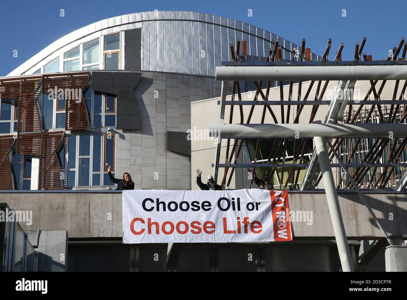 Three members of Extinction Rebellion Scotland who have climbed on to Holyrood, the Scottish Parliament in Edinburgh, and draped a banner reading 'Choose Oil or Choose Life' from an overhang above the public entrance in a protest against fossil fuels. Stock Photo
