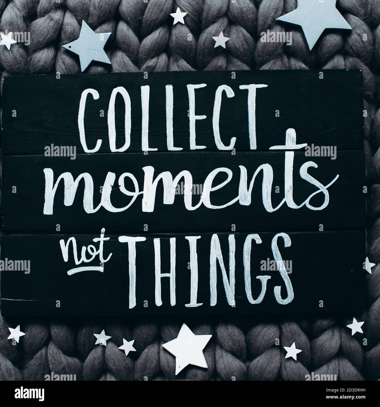 Black wooden board with the inscription collect moments not things and around the scattered stars on a gray cotton blanket of coarse knitting. Flat la Stock Photo