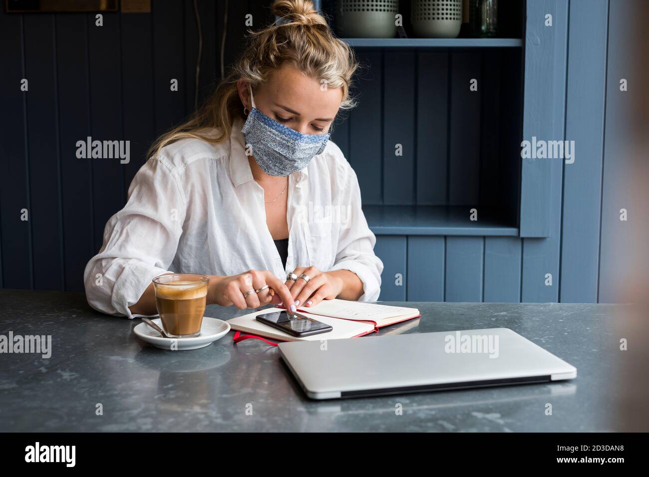 Woman wearing face mask alone at a cafe table with a laptop and ...