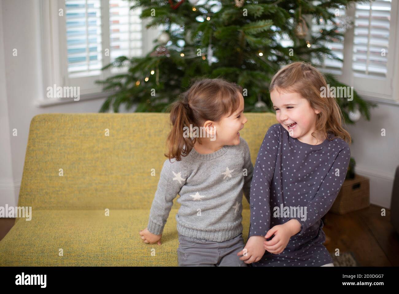 Two young girls sitting on sofa in living room, smiling at each other ...