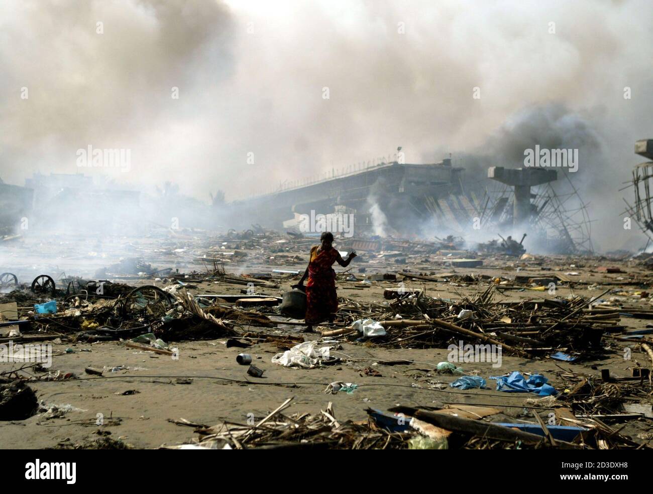 An Indian survivor walks through debris and burning parts of damaged fishing trawlers in Nagapattinam port, which was hit by Sunday's tsunami.  An Indian survivor walks through debris and burning parts of damaged fishing trawlers in Nagapattinam port, 350 km (219 miles) south of the Indian city of Madras December 29, 2004, which was hit by Sunday's tsunami. Rescue teams headed out on Wednesday to the last of the remote Andaman and Nicobar islands, cut off since Sunday's monster tidal wave triggered by an earthquake killed almost 70,000 people across Asia. Pictures of the month December 2004 RE Stock Photo