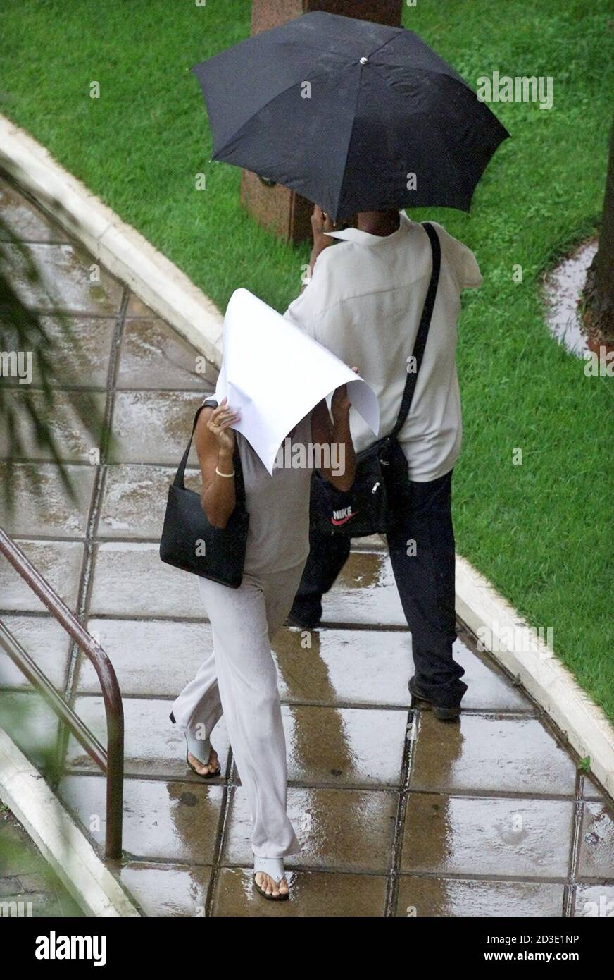 Caught in a downpour without proper cover, unlike the man behind her, a pedestrian uses a large envelope to shield herself in Brasilia March 20, 2001. Commuters were greeted with heavy rainfall on the first official day of Fall in the nation's capital.  GN/SV Stock Photo