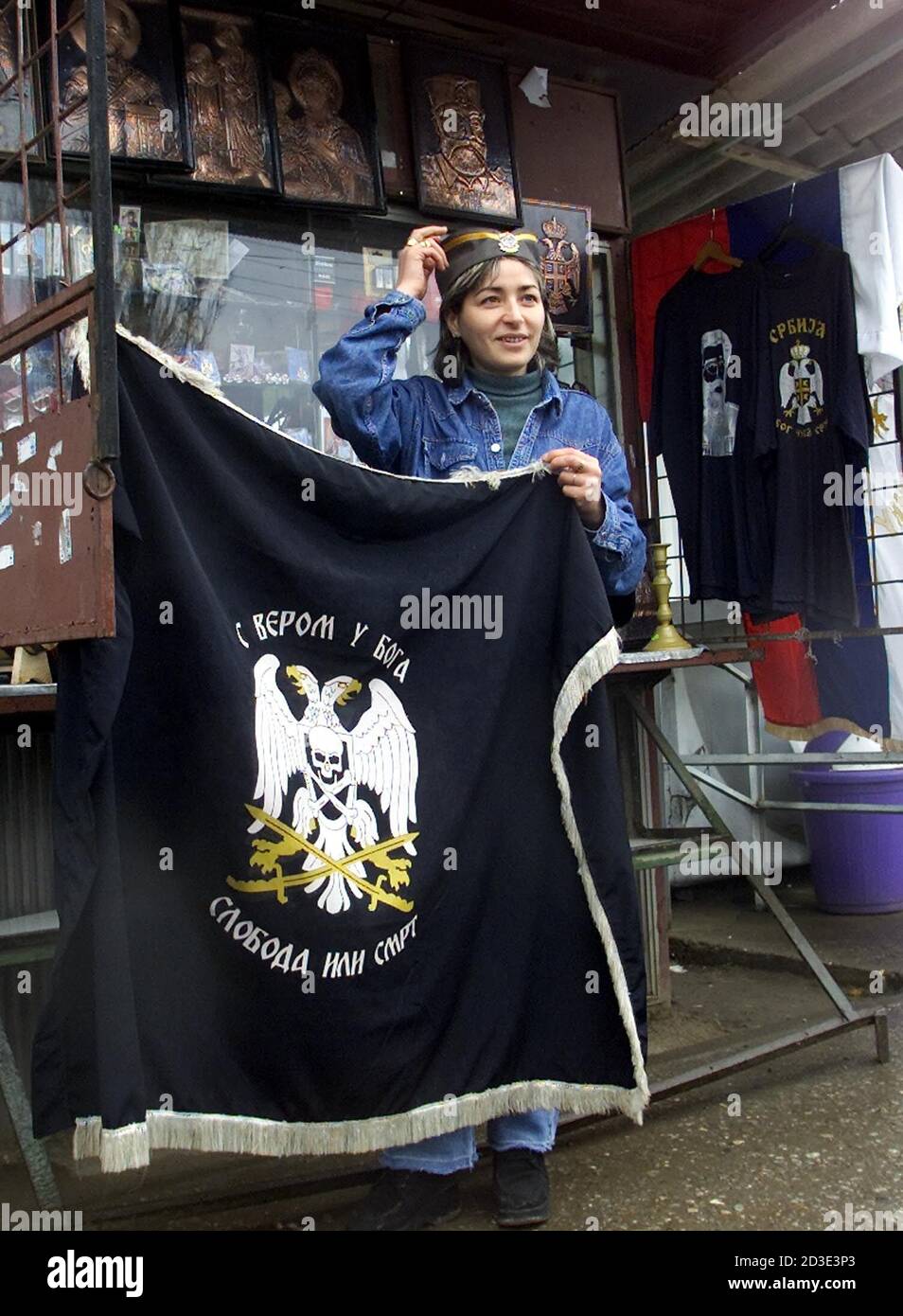 A Kosovo Serb girl tries on a traditional Cetnic hat holding a Serbian flag  November 14, 2001 in front of a memorabilia street shop in Gracanica, a  KFOR protected enclave near Pristina.