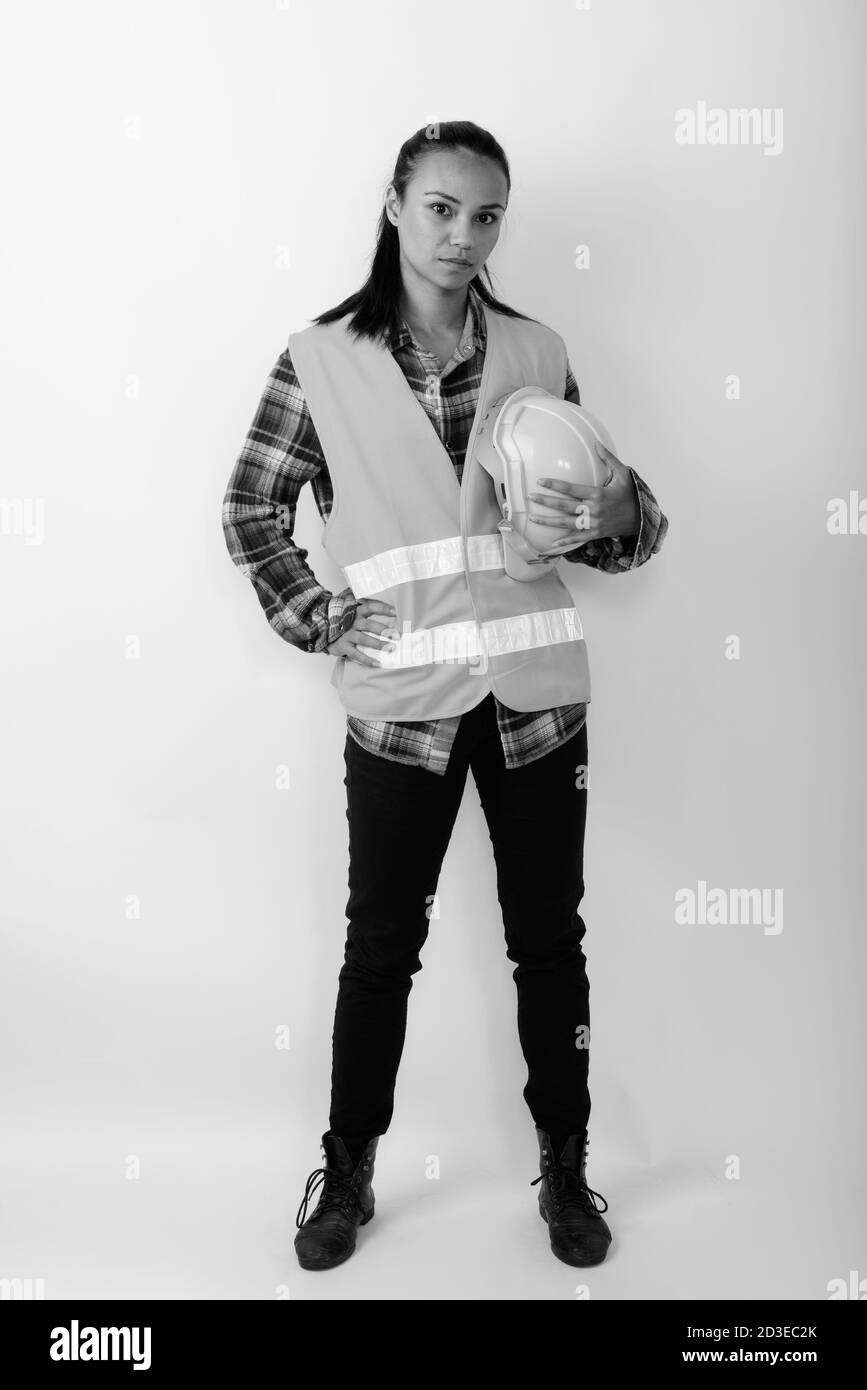 Full body shot of young Asian woman construction worker standing while holding hard hat Stock Photo