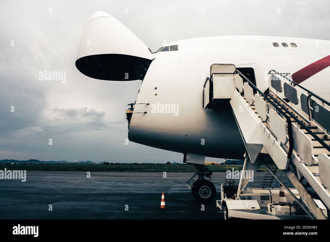 A Jumbo Jet freighter aircraft with a wide open nose cargo door waiting at a cargo ramp for a high-loader to be offloaded Stock Photo