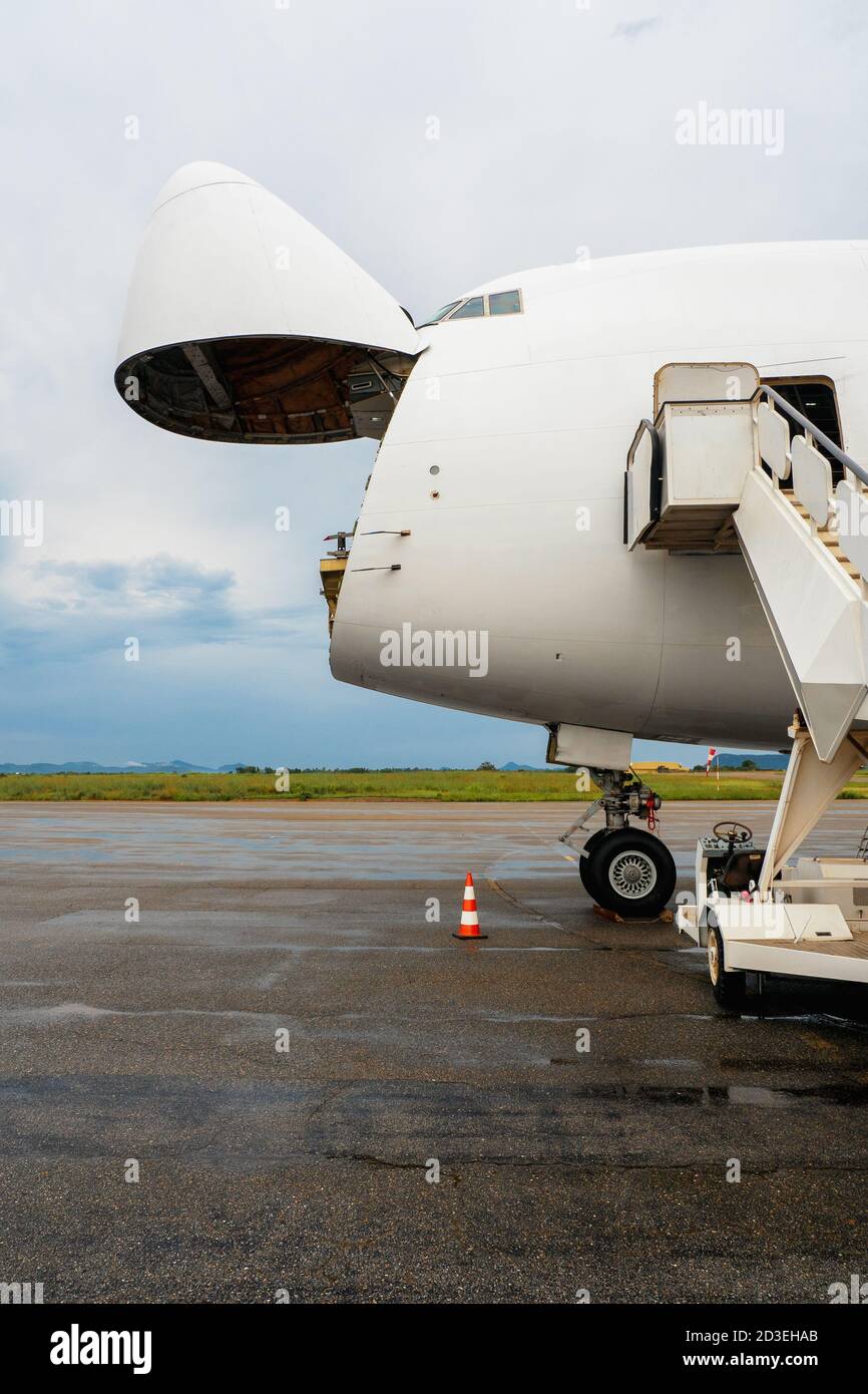 A Jumbo Jet freighter aircraft with a wide open nose cargo door waiting at a cargo ramp for a high-loader to be offloaded Stock Photo