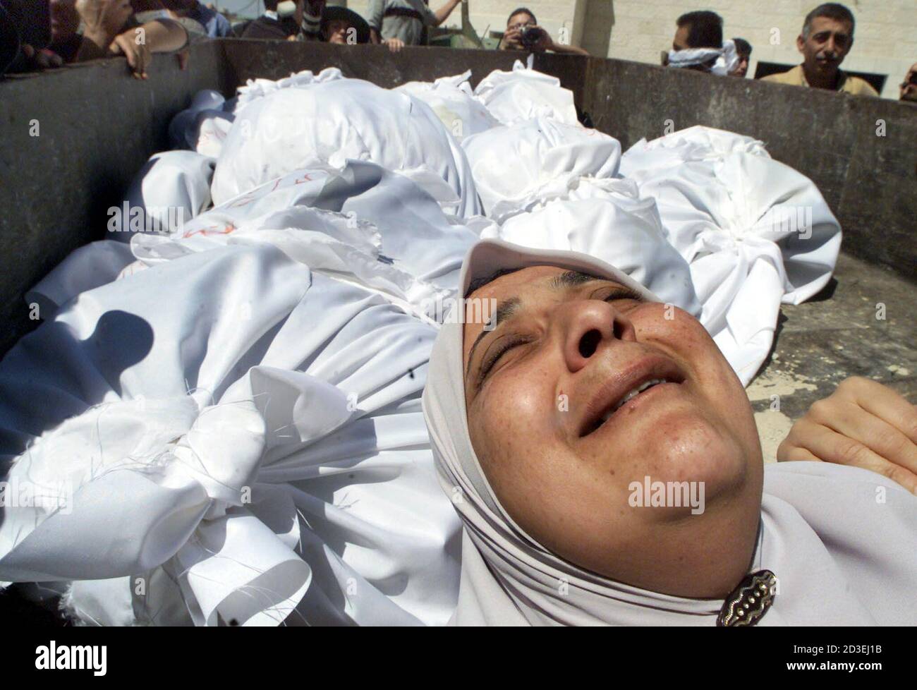 A Palestinian woman cries next to bodies of Palestinians killed in Jenin refugee camp April 19, 2002. [Thirty-five Palestinians swathed in white shrouds and some decked with purple flowers were buried on Friday in common graves in an olive grove on the edge of the Jenin refugee camp.  An Israeli army pullout earlier in the day brought no joy to residents of the camp, where so far 39 Palestinians have been confirmed killed in the worst violence of a West Bank blitz Israel launched after a spate of Palestinian suicide bombings] Stock Photo