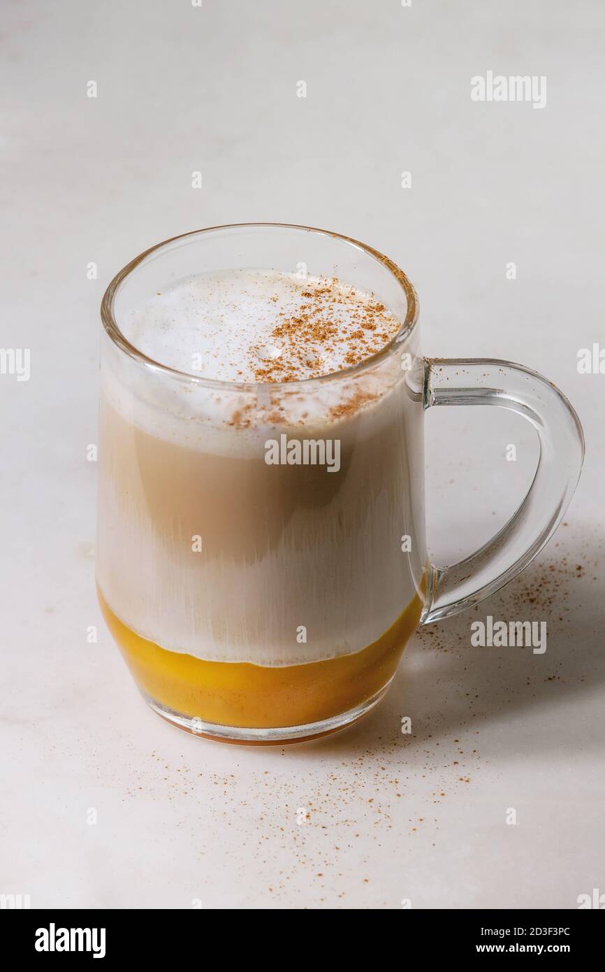 Glass of pumpkin layered spice latte with pumpkin puree, milk foam and cinnamon standing on white marble table. Close up Stock Photo