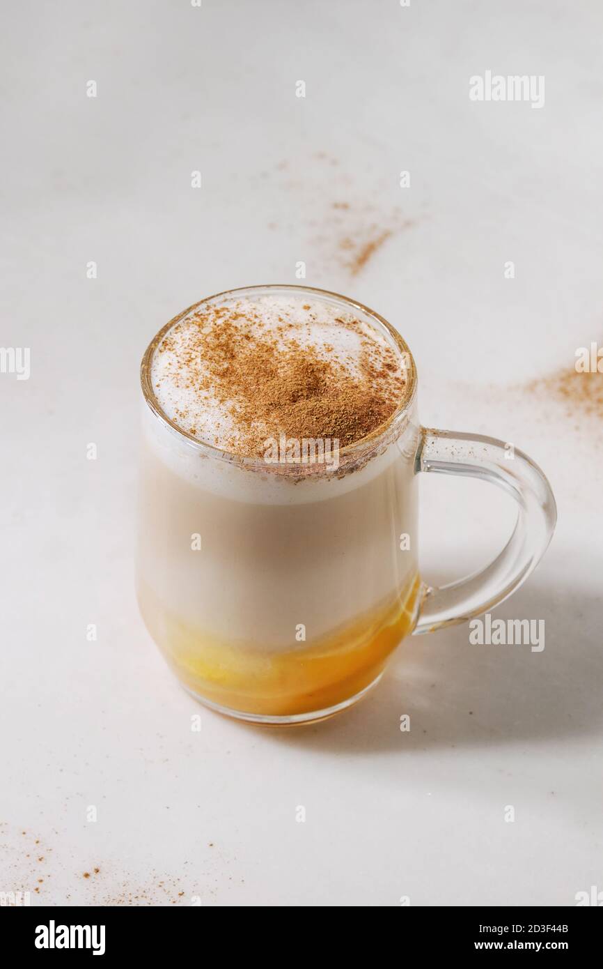 Glass of pumpkin layered spice latte with pumpkin puree, milk foam and cinnamon standing on white marble table. Copy space Stock Photo