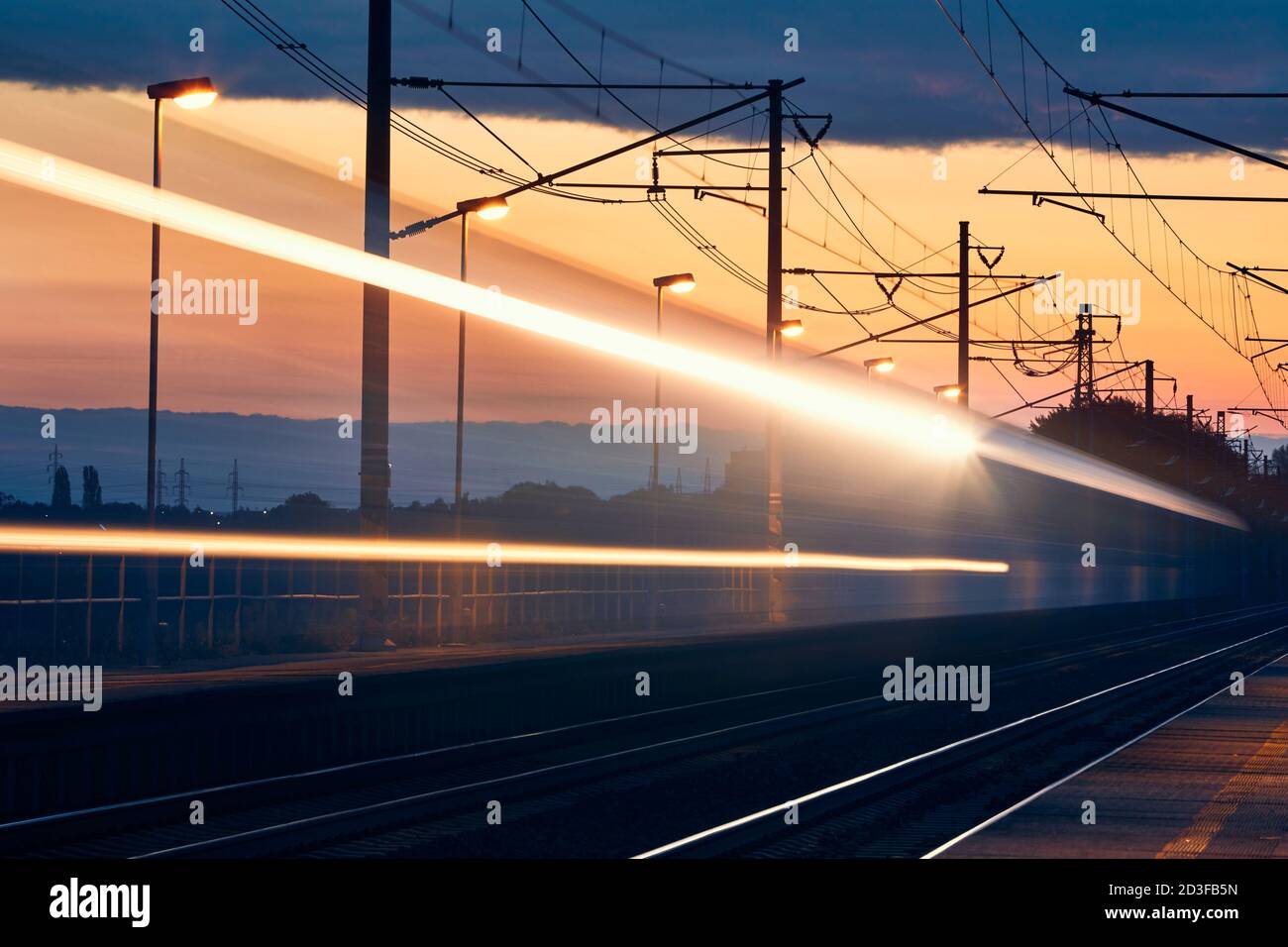 Railway at dawn. Light trails of passenger train at railroad station. Stock Photo