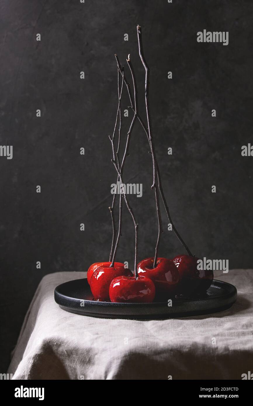 Red caramel apples sweet autumn or Christmas dessert served with branches in black ceramic plate on linen table cloth with grey wall at background. Da Stock Photo