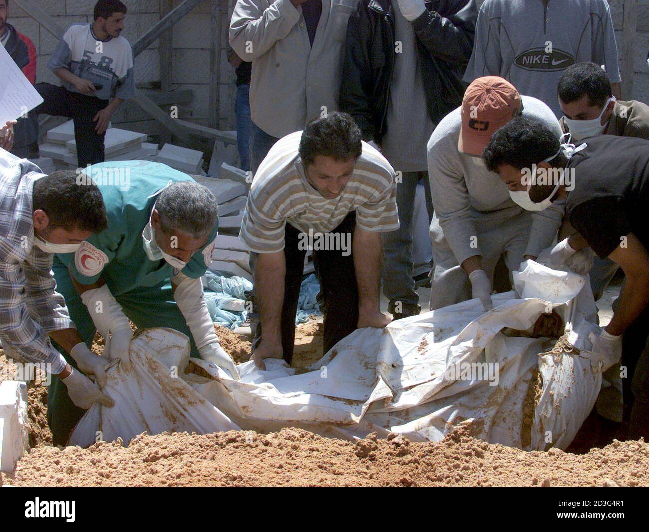 Palestinians bury dead bodies of Palestinians killed in Jenin refugee camp April 19, 2002.  [Thirty-five Palestinians swathed in white shrouds and some decked with purple flowers were buried on Friday in common graves in an olive grove on the edge of the Jenin refugee camp.  An Israeli army pullout earlier in the day brought no joy to residents of the camp, where so far 39 Palestinians have been confirmed killed in the worst violence of a West Bank blitz Israel launched after a spate of Palestinian suicide bombings] Stock Photo