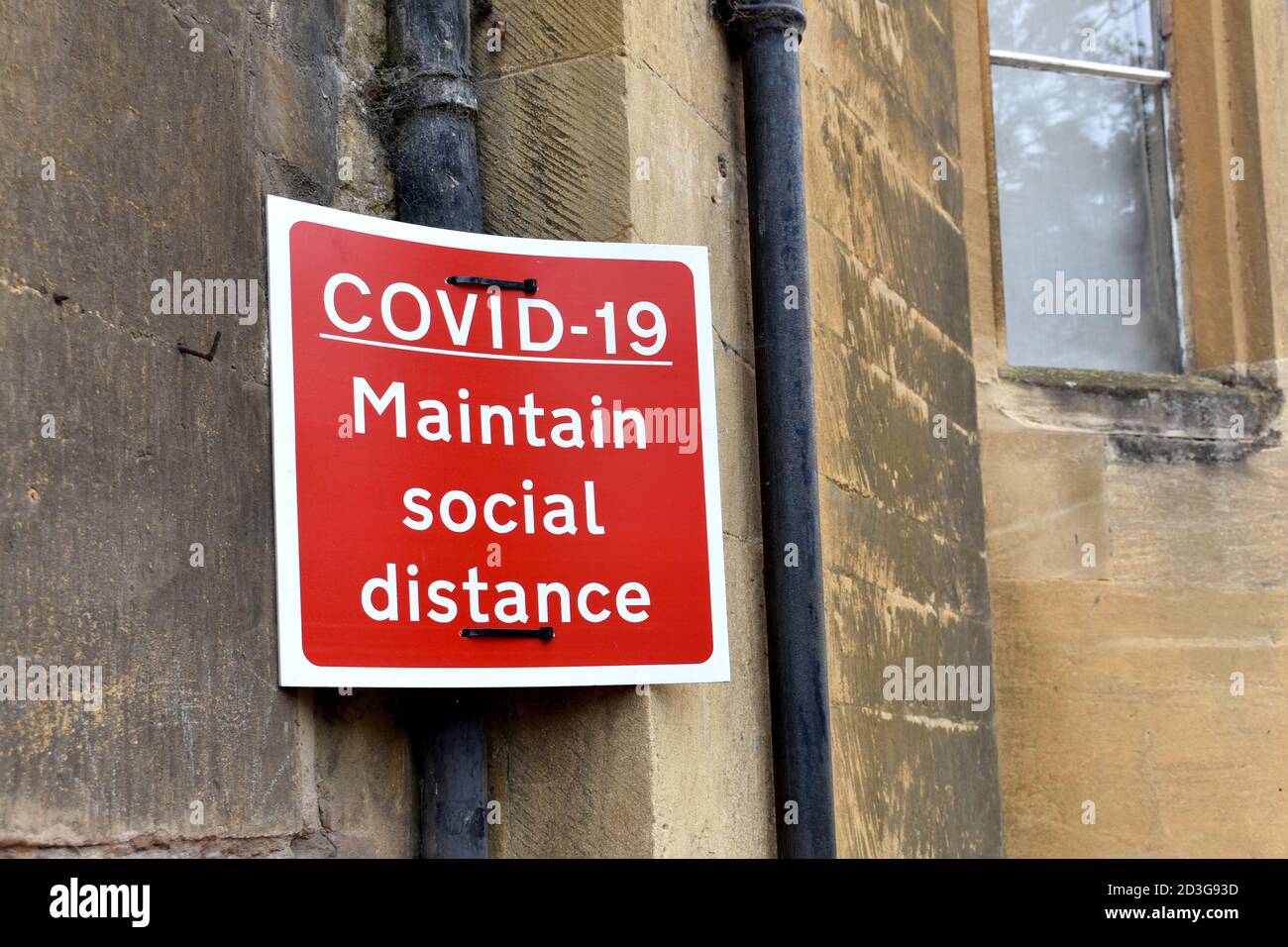 close up of red and white COVID-19 social distance sign outside on stone wall building with window Stock Photo