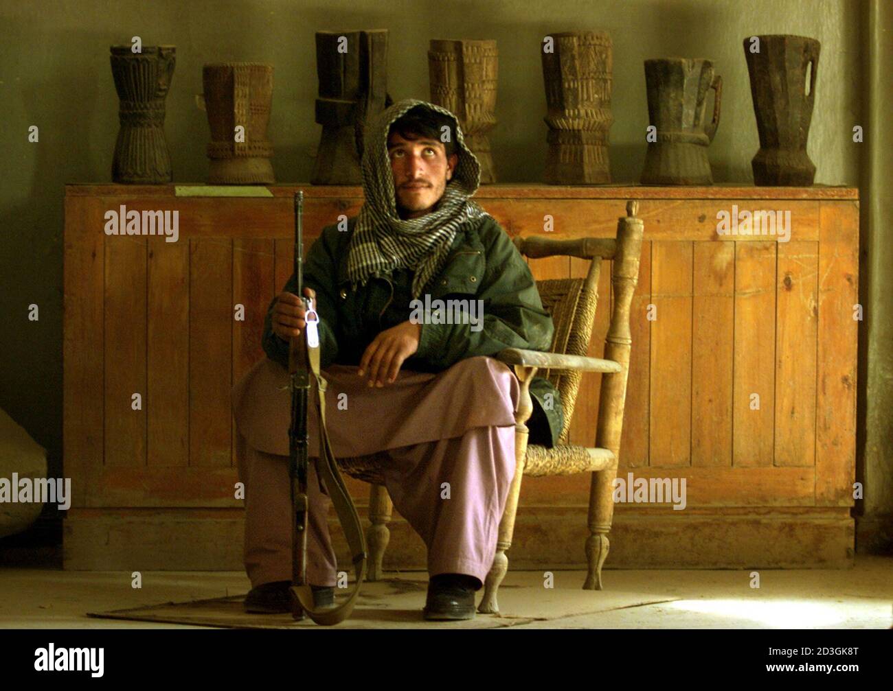 An Afghan soldier sits with his rifle guarding the entrance to Afghanistan's national museum in Kabul December 1, 2001. A pile of masonry in a dusty storeroom of Afghanistan's national museum is all that is left of several ancient statues. Two millennia old, they were hacked to pieces by the Taliban's religious police in just two days. Stock Photo