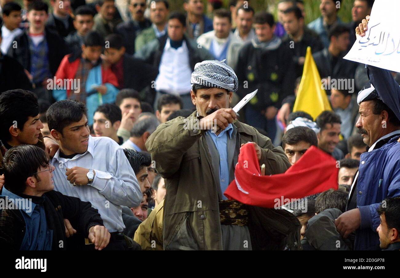 An Iraqi Kurd cuts a Turkish flag during a demonstration to protest possible Turkish intervention in the event of war, in Arbil, northern Iraq March 3, 2003. Thousands of Iraqi Kurds took to the streets in protest at Turkish plans for military intervention in northern Iraq, but police said it passed off peacefully. REUTERS/Caren Firouz  CJF/jm Stock Photo