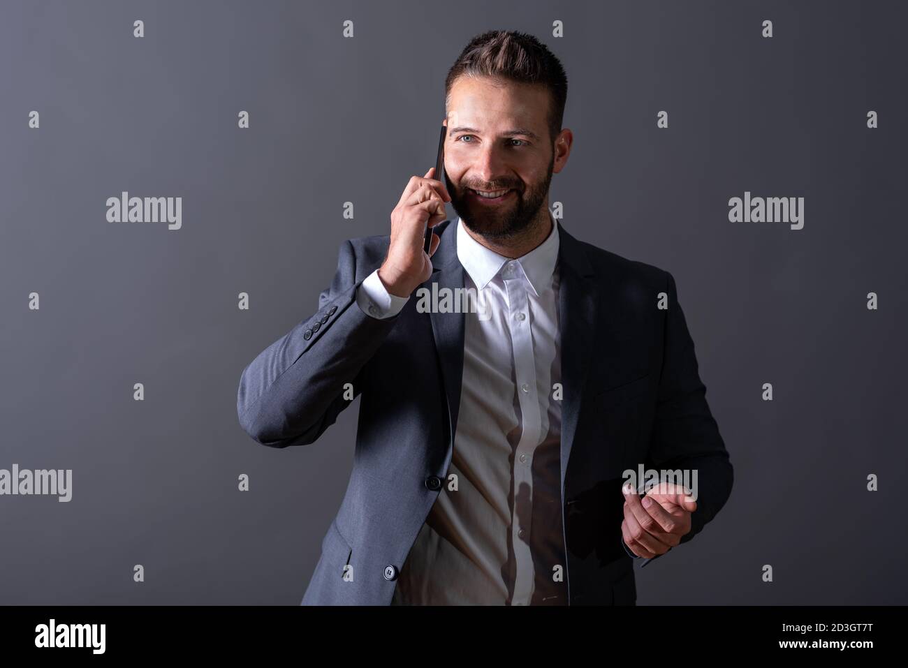 A smiling handsome young businessman in a suit talking on his phone in ...