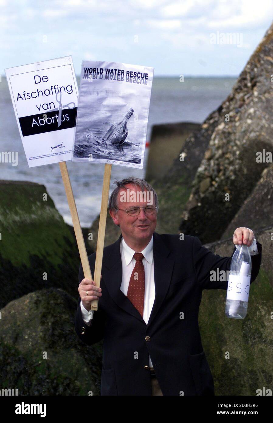 President of the Cry for Life movement Bert Doorenbos holds a bottle containing an anti abortion message into the sea as he holds two banners one reading ' abolition of abortion ' at The Dutch Port of Hoek van Holland, as a protest to the departure of  the Dutch abortion ship Aurora, rechristened the Sea of Change, June 11, 2001. The ship offering onboard abortions departed for Ireland facing a likely wave of protests  and the threat of legal actions at home. The ship, a converted fishing boat rechristened the Sea of Change, pushed off from its berth beside a Greenpeace vessel in the Dutch sma Stock Photo