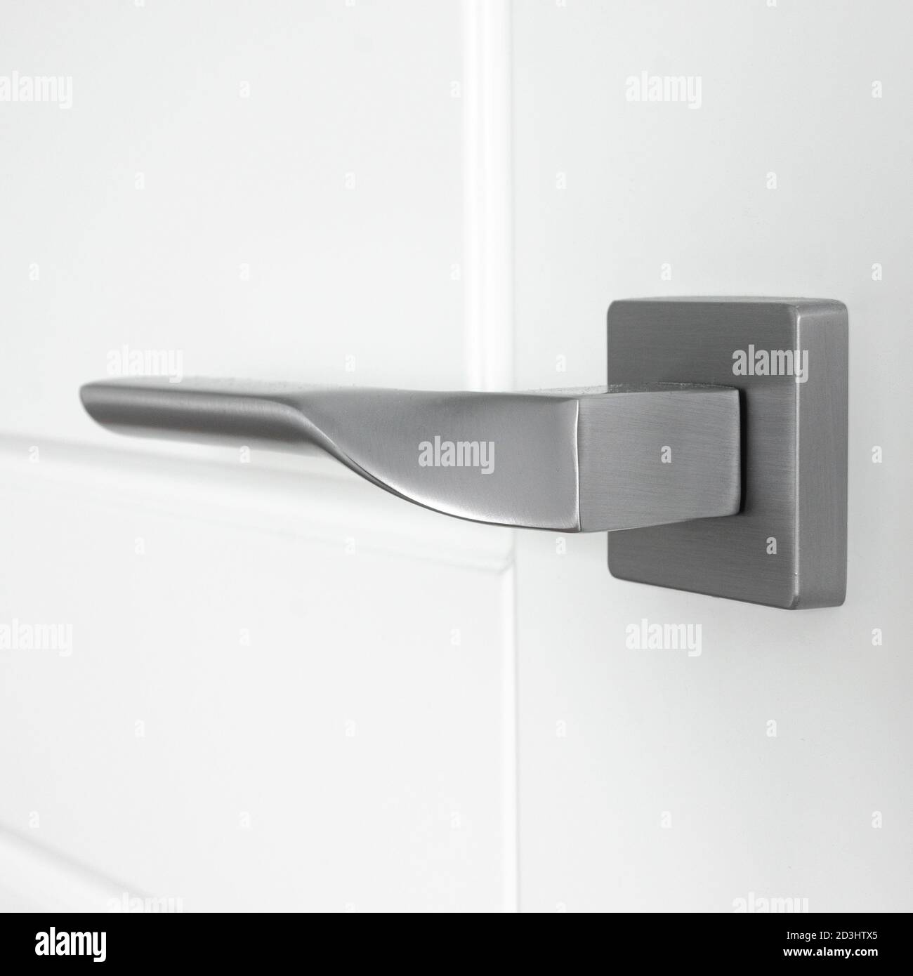 The silver metal doorknob is mounted in a white wooden door Stock Photo