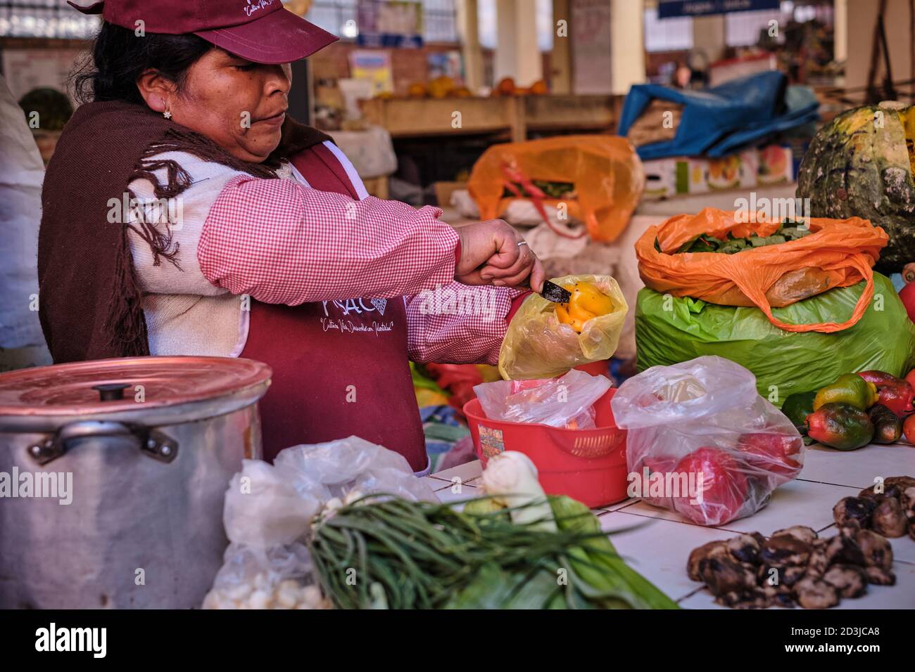Woman female stallholder at Pisac Pisaq Market, Peru, preparing a yellow pepper capsicum on her vegetable stall Stock Photo