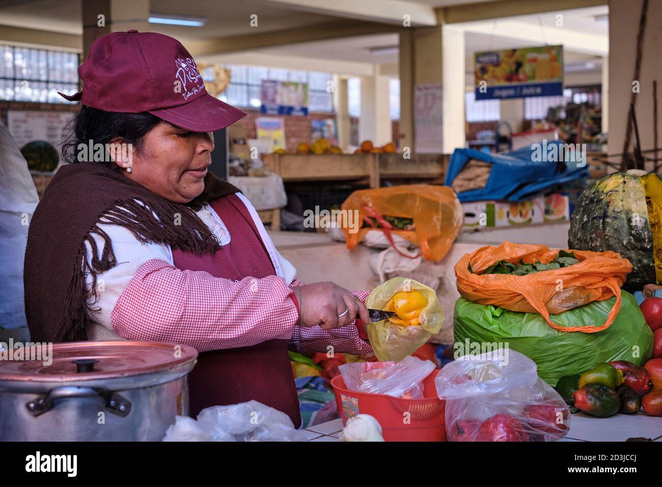 Woman female stallholder at Pisac Pisaq Market, Peru, preparing a yellow pepper capsicum on her vegetable stall Stock Photo