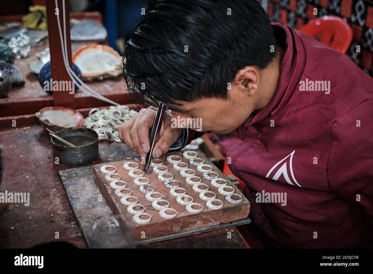 A silversmith jeweller in Pisac Pisaq Market, Peru, making earrings jewellery jewelry. He is holding forceps tweezers and concentrating on his work Stock Photo