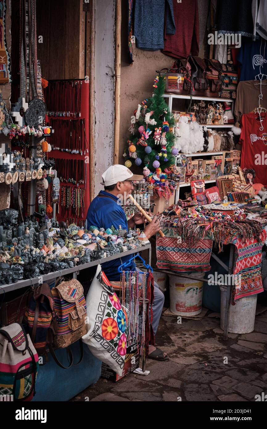 Pisaq Market Pisac smallholder playing on a recorder or similar woodwind instrument to attract tourist customers. He is surrounded by colourful gifts Stock Photo