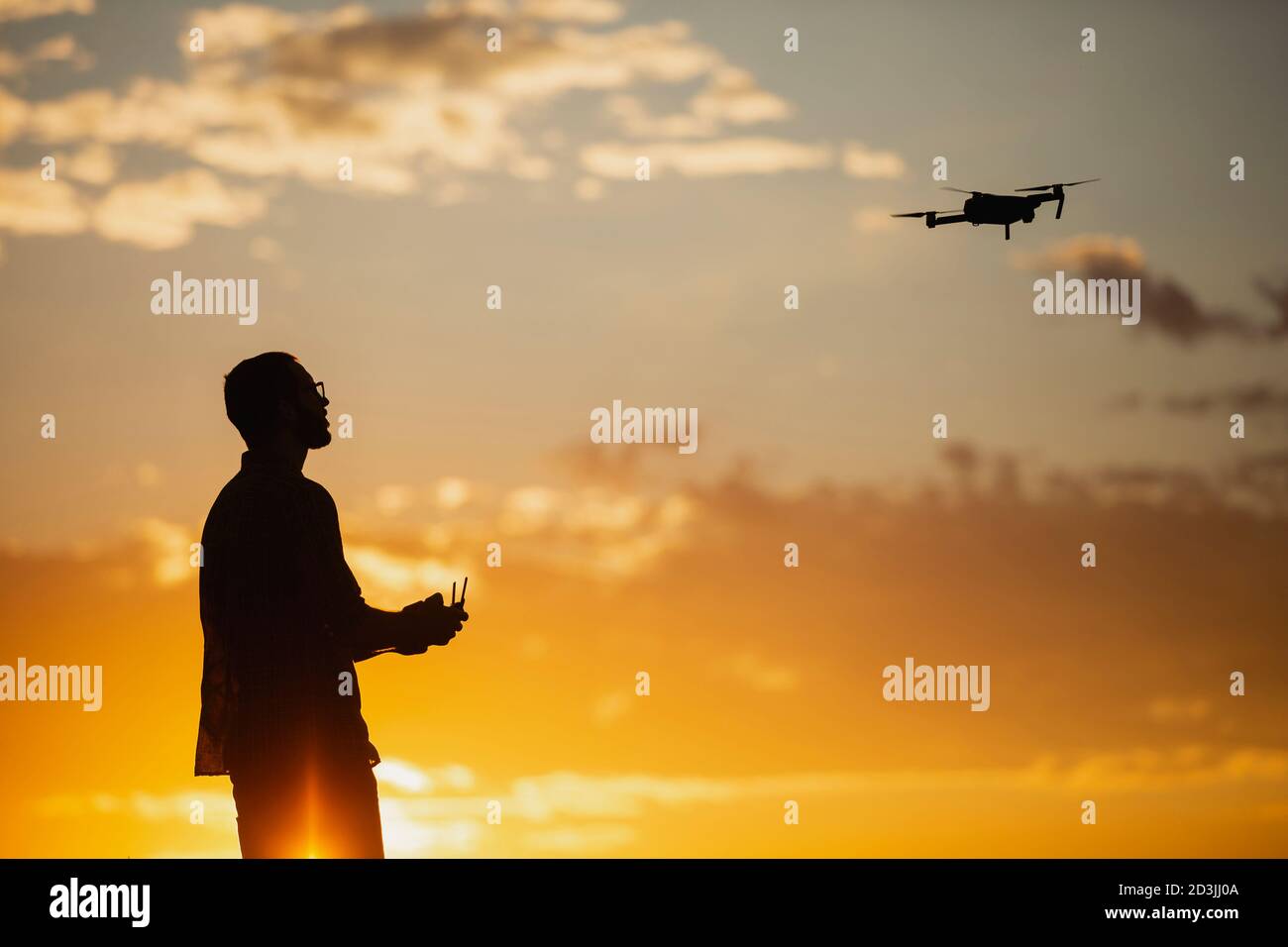 Silhouette of a young man operating a drone in A Rural Setting on sunset Stock Photo