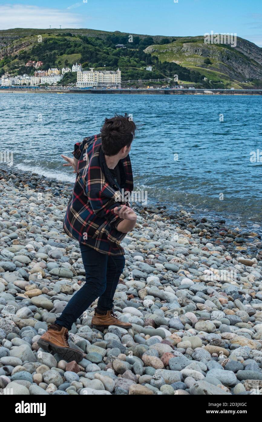 Man throwing pebbles into the sea at Llandudno North Shore beach Stock Photo