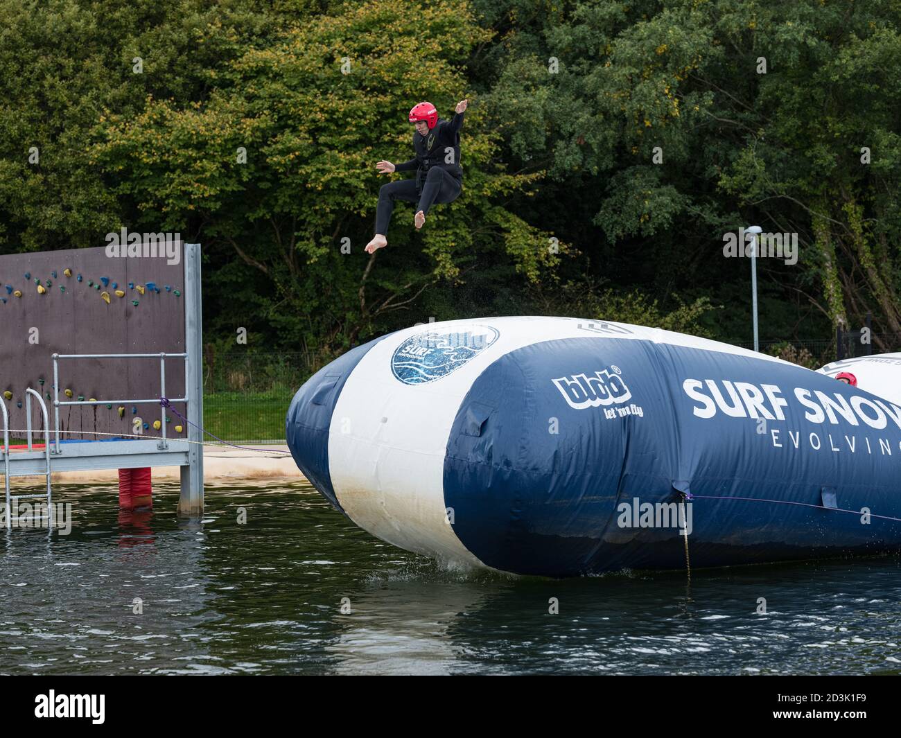An adventurous lady bouncing off the airbag into the pool at Surf Snowdonia, Wales Stock Photo