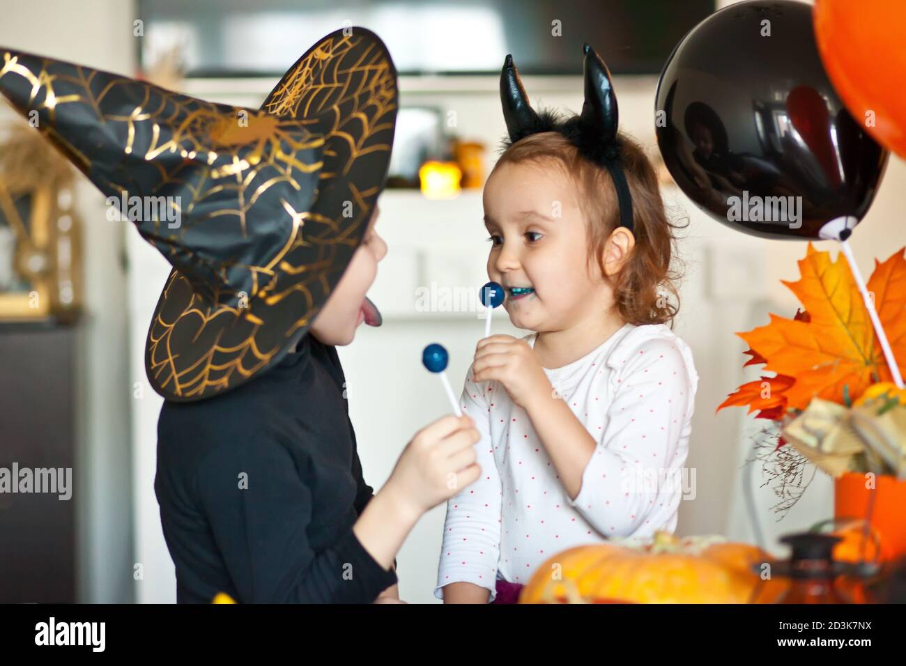 funny child girl and boy in witch and evil costumes for Halloween eating candies lolly pops and have fun. Stock Photo