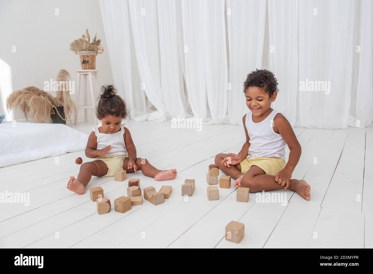 Little Brother and Sister African American play houses with wooden eco bricks, build and destroy towers. Fine motor development, educational games. Wh Stock Photo
