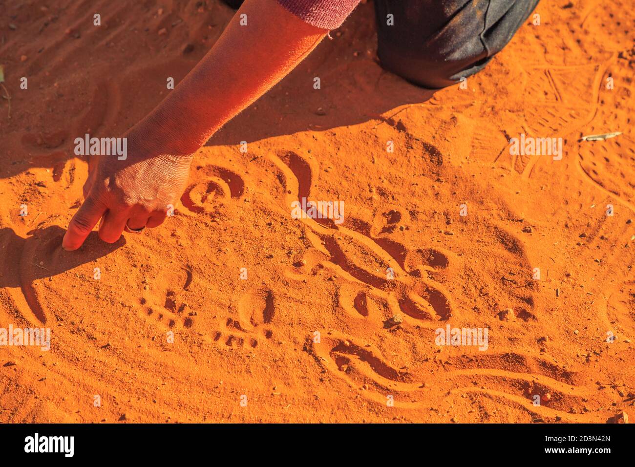 Kings Creek Station, Northern Territory, Australia - Aug 21, 2019: aboriginal woman hands creating shapes with red sand on the ground in aboriginal Stock Photo