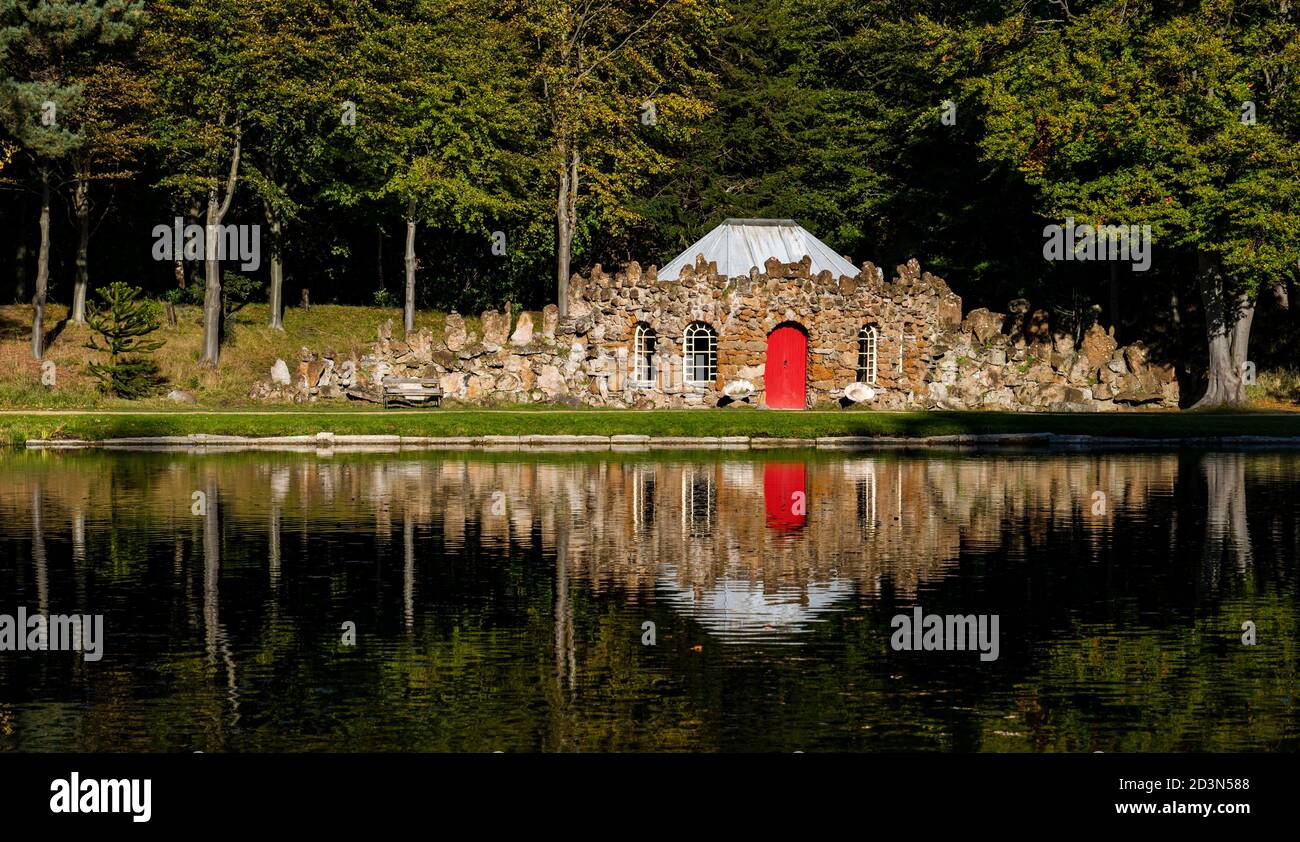 Gosford Estate, East Lothian, Scotland, United Kingdom, 8th October 2020. UK Weather: Autumn sunshine reflections. The quirky rubble stone curling lodge surrounded by Autumn trees is reflected in the artificial lake Stock Photo
