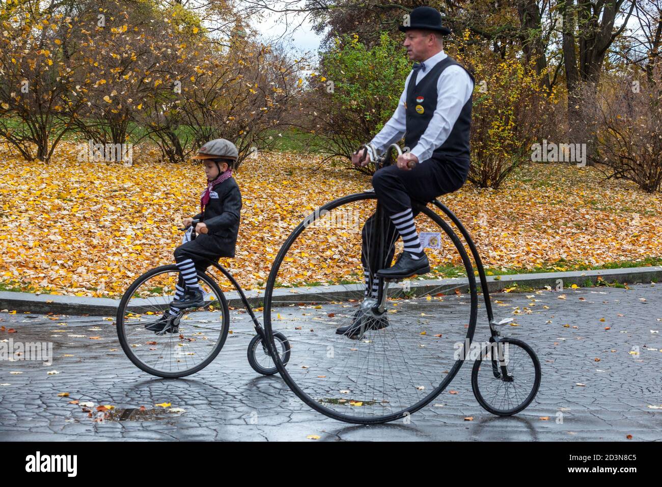 Two cyclists, man riding penny-farthing bicycle child people traditional period dress costume Stock Photo