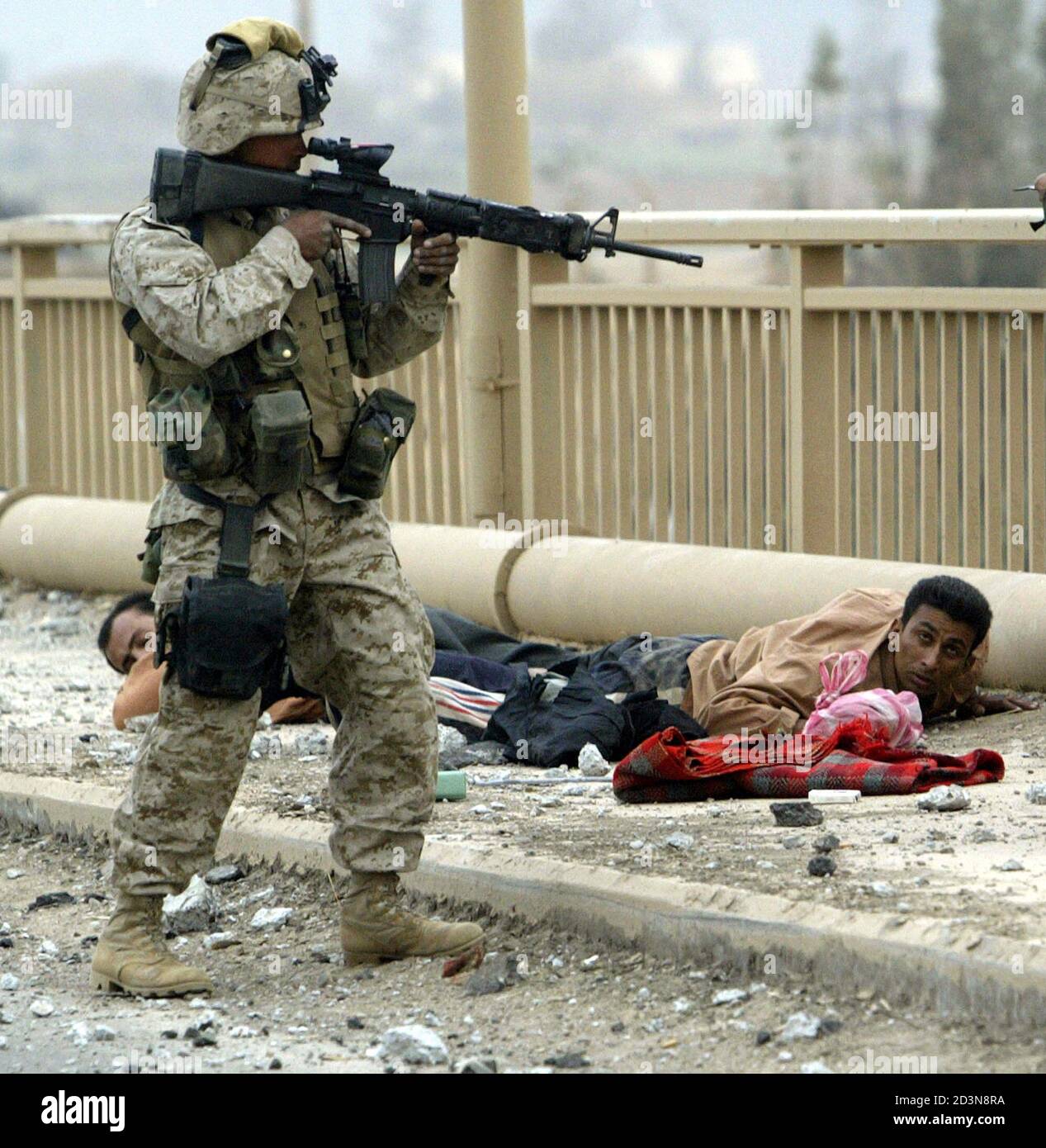 A U.S. Marine from Lima Company, a part of the 7th Marine Regiment, keeps two members of the Iraqi Republican guard dressed in civilian clothes on the ground on the New Baghdad highway bridge in the suburbs of the Iraqi capital Baghdad on April 7, 2003.  [U.S. forces burst into the heart of Baghdad on Monday and entered two palace complexes of President Saddam Hussein, but they said the operation was an armoured raid not intended to hold territory.] Stock Photo