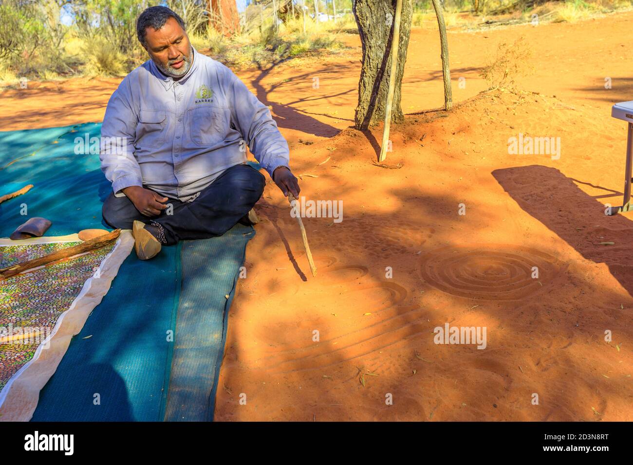 Kings Creek Station, Northern Territory, Australia - Aug 21, 2019: aboriginal guide man creating shapes with red sand on the ground in aboriginal art Stock Photo