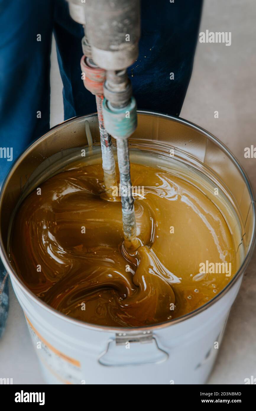 Worker mixing yellow epoxy resin with the mixer in a tin bucket Stock