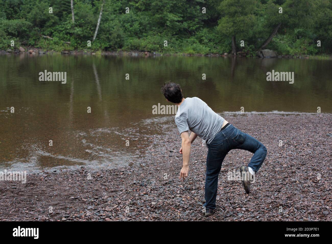 A young man throwing a rock into a lake. Stock Photo