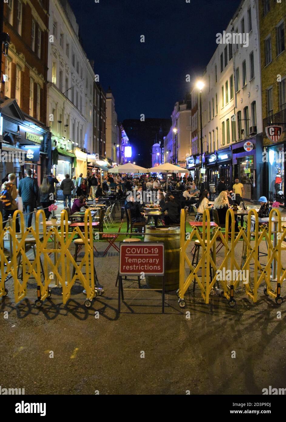 Crowd of people at night on Old Compton Street with Covid-19 traffic restriction sign, Soho, London 2020. Sections of Soho have been blocked for traffic to allow temporary outdoor street seating for bars and restaurants to facilitate social distancing during the pandemic. Stock Photo