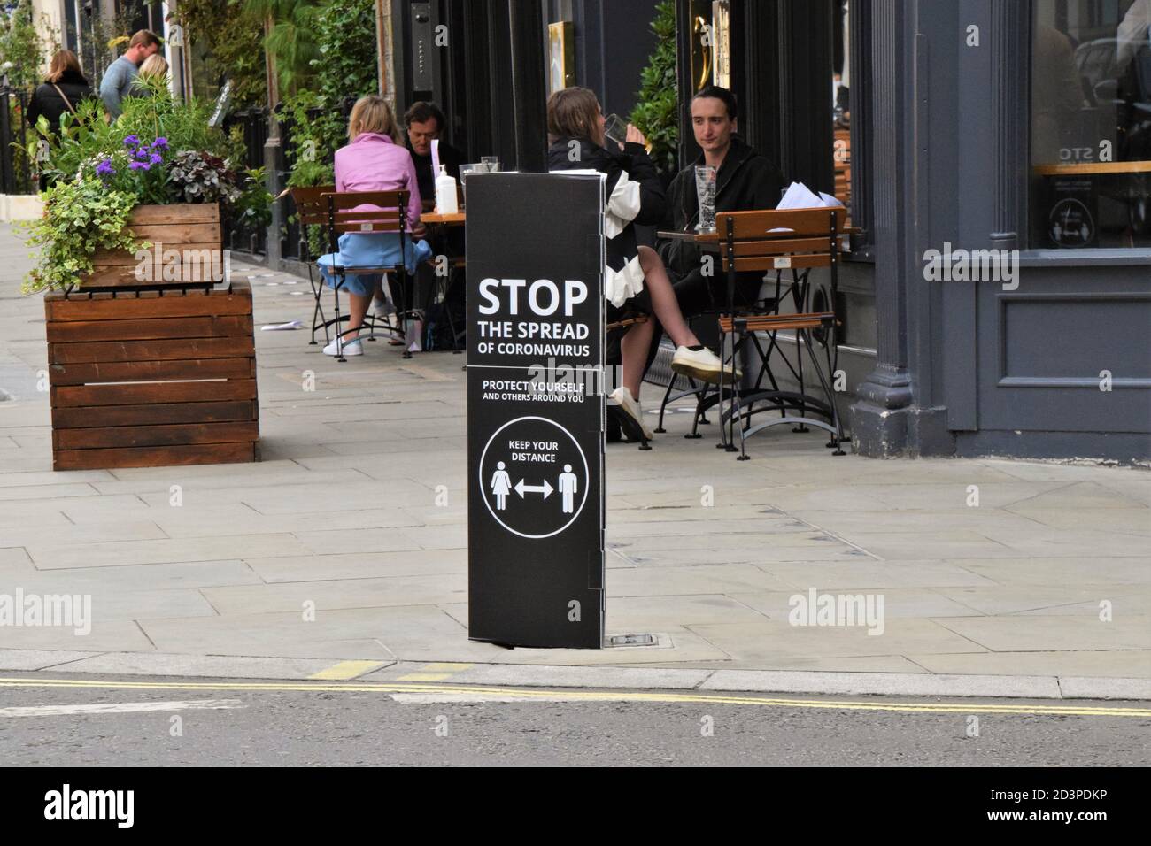 People walking past a Stop The Spread of Coronavirus street sign in Covent Garden, London, 2020. Signs have been placed all around Covent Garden streets and market to encourage social distancing. Stock Photo