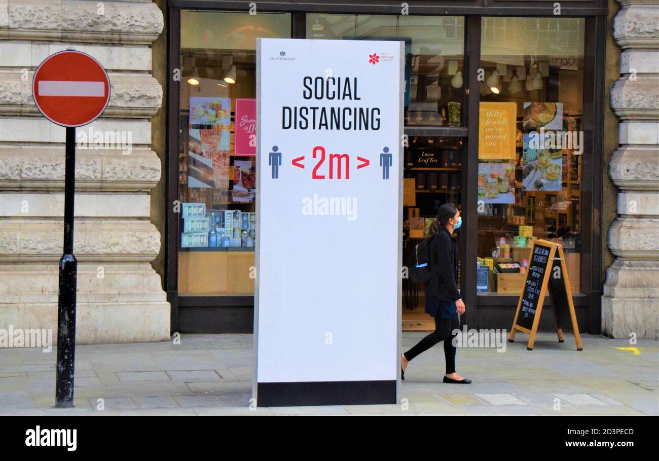 A woman with a protective face mask walks past a social distancing street sign on Regent Street, London, 2020. Stock Photo
