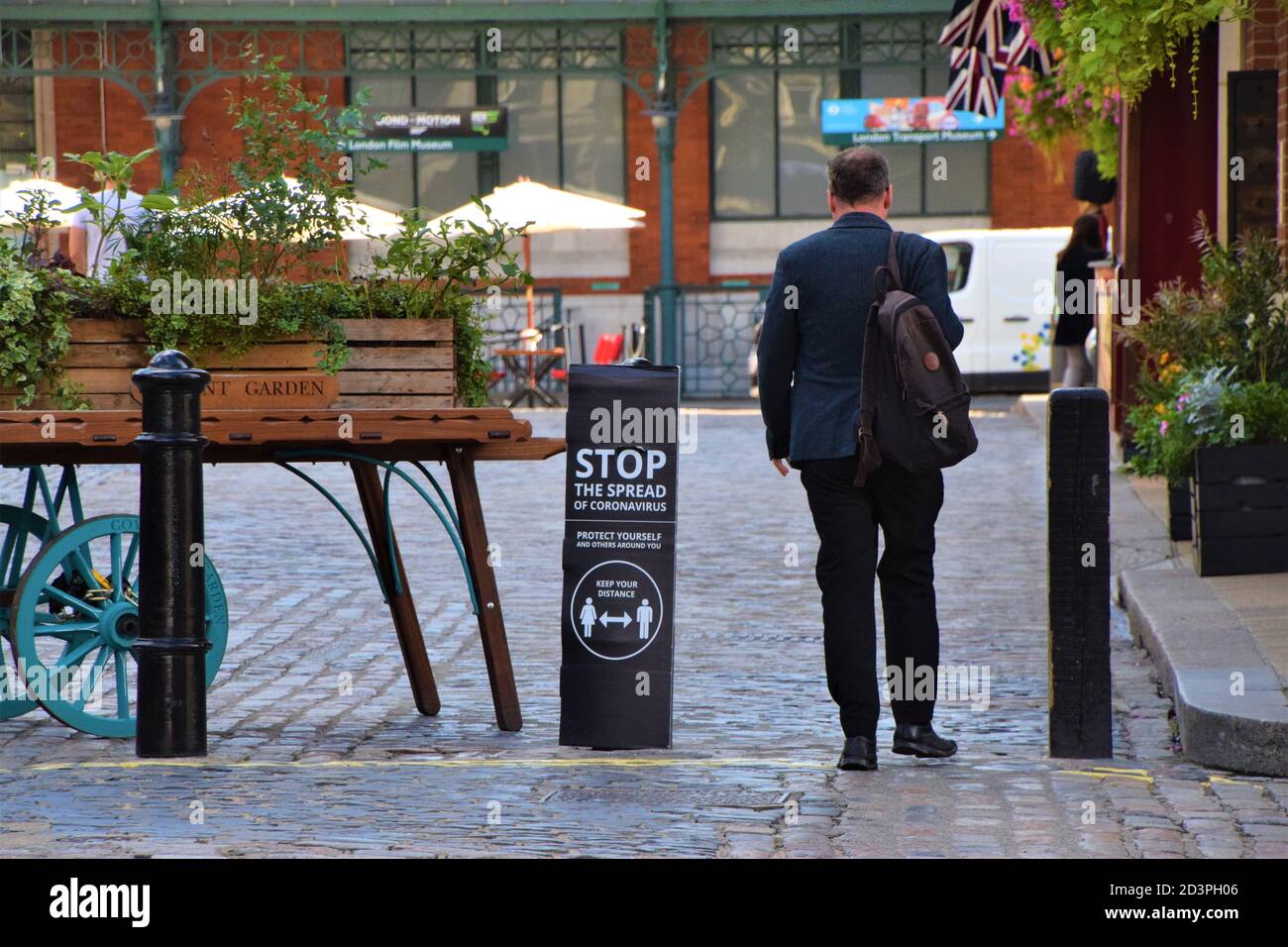 A man walks past a Stop The Spread of Coronavirus street sign in Covent Garden, London, 2020. Signs have been placed all around Covent Garden streets and market to encourage social distancing. Stock Photo
